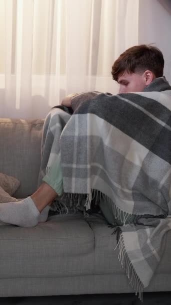 垂直录像 病毒感染 生病的男人 家庭健康治疗 闷闷不乐的家伙裹着毛毯坐在沙发上 在客厅里咳嗽发烧 — 图库视频影像