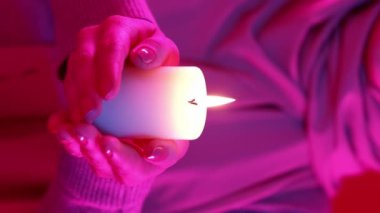 Dikey video. Mum duası. İslami selamlaşma. Ramazan Kareem. Tanımlanamayan kadın elleri parlak pembe neon ışığıyla yanan balmumu alevi tutuyor..