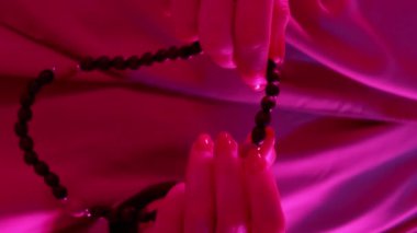 Dikey video. Boncuklar dua ediyor. Tasbih geleneği. Tanınmayan kadın elleri ahşap tespih, İslami inanç, pembe neon ışık..
