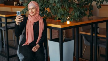 Görüntülü arama. Vlog kaydı. Güzel kadın tesettürde etkili oldu akıllı telefon internet iletişimiyle konuşuyor rahat kafede canlı sohbet..