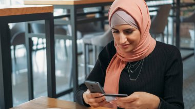 Mobil alışveriş. Dijital ödeme. Keyifli bir kadın internet üzerinden alışveriş yapıyor. Akıllı telefonlu internet mağazasından. Telefon bankacılığı kafede oturuyor..