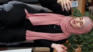 Dikey video. Çevrimiçi çağrı. Vlog kaydı. Güzel kadın tesettürde etkili oldu akıllı telefon internet iletişimi ile konuşuyor rahat kafede canlı sohbet.