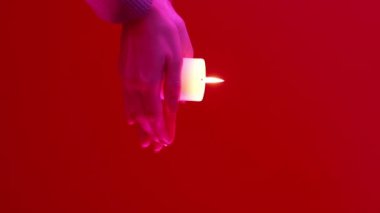 Dikey video. Ramazan ayini. İslam dini. Kırmızı fotokopi arkaplanındaki pembe neon ışıkta yanan mum ışığını tutan tanınmayan kadın elleri.