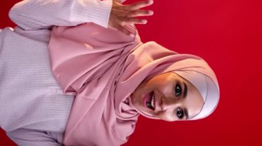Dikey video. Zafer vay canına. Başarı sevinci. Olumlu tepki. Kırmızı fotokopi arkaplanına izole edilmiş, mutlu, mutlu, mutlu, başörtülü kadın..
