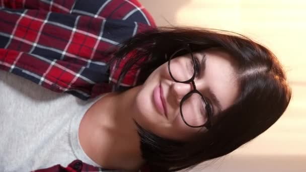 バーティカルビデオ スマートな女性 笑顔の肖像画 積極的な姿勢 明るい部屋のインテリアに座る光景で陽気なカジュアルな女性学生 — ストック動画