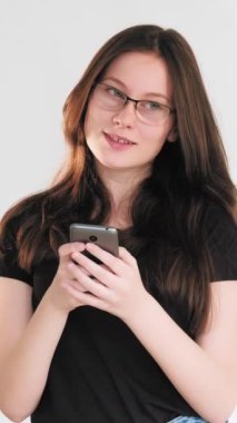 Dikey video. Romantik sohbet. Çevrimiçi flört. Mesafe iletişimi. Aşık bir kadın cep telefonundan mesaj okuyor. Beyazlar arasında izole edilmiş..