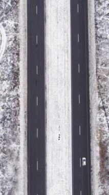 Dikey video. Hava karlı yolu. Kış manzarası. Beyaz donmuş orman ağacı asfalt şeritli, geçen arabalar bulutlu kırsal yol kaldırımlı..