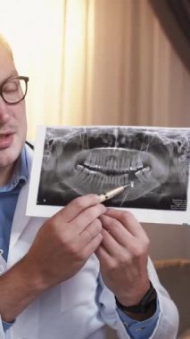 Dikey video. Diş hekimi konsültasyonu. Diş röntgeni. Ağız röntgeni filmli profesyonel bir doktor kliniğin iç kısımlarında teşhis koyuyor..