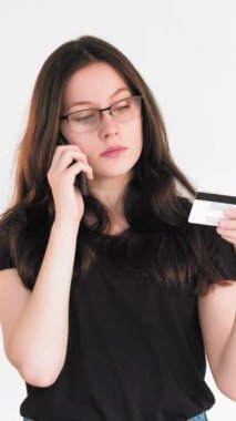 Dikey video. Banka dolandırıcılığı. Ödeme riski. Kafası karışmış şüpheci bir kadın kredi kartı bilgilerini beyaz telefondan aktarıyor..