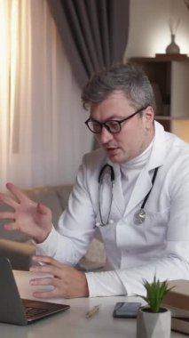 Dikey video. Teletıp çağrısı. İnternet randevusu. Modern çalışma masasında laptopta danışmanlık yapan beyaz üniformalı, pozitif sağlık uzmanı..