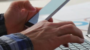 İş teknolojisi. Dijital çalışma. Ofisteki adam cep telefonunda e-posta gönderiyor ve modern işyerindeki dizüstü bilgisayarında proje verileri yazıyor..