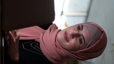 Dikey video. Uzaktan kumanda. Serbest çalışan biri. Gülümseyen, tesettürlü, tesettürlü, dizüstü bilgisayarda yazan, kahve dükkanındaki interneti karıştıran iş kadını..