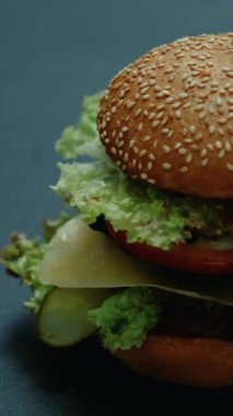 Dikey video. Sağlıksız burger. Fast food. Lezzetli hamburger, Amerikan mutfağı abur cubur, çizburger koyu arka planda izole edilmiş..