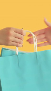 Dikey video. Alışveriş teslimatı. Perakende satış. Kadın müşteri eli Kara Cuma sezonu indirimini alıyor. Kağıt çantalar. Turuncu arka planda ayrılan hediye..