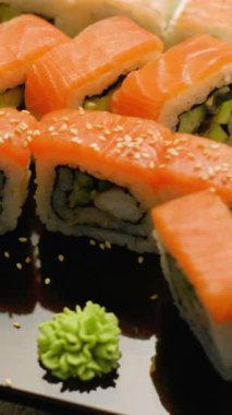 Dikey video. Lezzetli suşi. Japon yemeği. Lokantada susam ile süslenmiş somon dürümleri koyu arka planda..