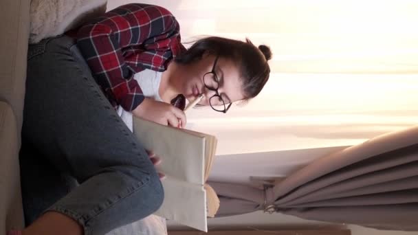 バーティカルビデオ 研究問題 試験準備をする ホーム教育について 混乱した女性読書 宿題に不満 座っているソファールームのインテリア — ストック動画