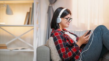 Mobil müzik. Şarkı dinlemede. Gadget 'ın boş vakti. Kulaklıklı tatmin olmuş bir kadın evdeki rahat koltukta telefon çalma listesinin keyfini çıkarıyor..