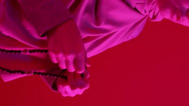 Dikey video. İslami dua. Geleneksel tasbih. Tanınmaz halde, ahşap tespih boncukları ve parlak pembe neon ışığı olan bir kadın..