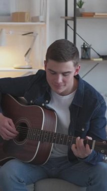 Dikey video. Profesyonel müzisyen. Gitar sanatçısı. Yetenekli bir müzisyen, evdeki oturma odasında ip akustik enstrüman çalıyor..