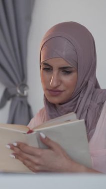 Dikey video. Boş vakitleri değerlendiriyorum. Edebiyat hayranıyım. Bilgi çalış. Huzurlu, huzurlu, gülümseyen kadın evde en çok satan kitap hobisinin tadını çıkarıyor..