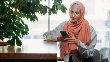 Gezici blog yazma. Kahve keyfi. Tesettürlü, tesettürlü, sosyal medya mesajları atan, internette sohbet eden, rahat kahve dükkanında dinlenen bir kadın..