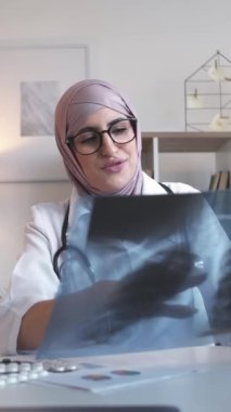 Dikey video. İnternet tıbbı. Uzaktan kumandalı. TeleHealth teşhisi. Kadın doktor klinikteki internet aramasında zatürree tedavisi için akciğer röntgeni danışmanlığını inceliyor..