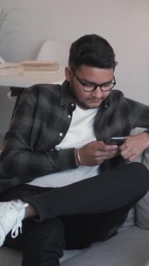 Dikey video. Telefon eğlencesi. İnternet sohbeti. Çevrimiçi boş zaman. Neşeli adam akıllı telefondan mesaj atıyor sosyal medya evdeki kanepede dinleniyor..