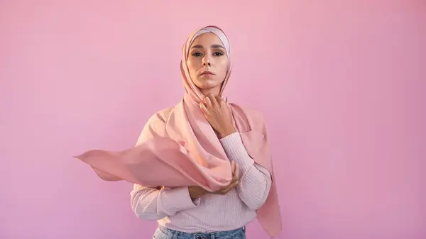 Hijab fashion. Female accessories. Glamour muslim. Confident woman covering head wearing silk headscarf traditional islamic outfit isolated on pink empty space background.