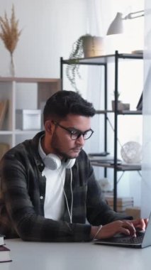 Dikey video. Uzaktan eğitim. Ev ödevi. Mesafe öğrenme. Bilgisayarda daktilo kullanan ciddi odaklı bir adam. Masa başı işyerinde ödev üniversitesi araştırması yapıyor..