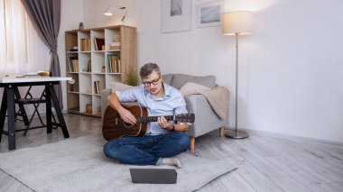 Müzisyen öğrenci. İnternetten ders. Evde eğitim. Akıllı konsantre adam, akustik gitar akorları üzerinde çalışıyor. Oturma odasındaki dizüstü bilgisayarın video toplantısında oturup fotokopi çekiyor..