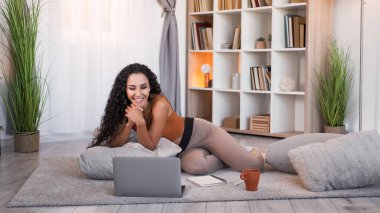 Çevrimiçi boş zaman. İnternet eğlencesi. Rahatlamış neşeli kız dizüstü bilgisayarında film izlemekten zevk alıyor modern ev oturma odasının içinde boş yer var..