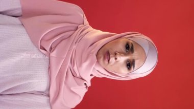 Dikey video. Korkmuş yüz. Omg paniği. Şok edici bir haber. Ağzı örten tesettürlü, korkmuş, endişeli kadın kırmızı fotokopi arkaplanda izole edilmiş..