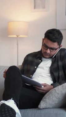 Dikey video. İş görüşmesi. Başlangıç tartışması. Mobil iletişim. Ciddi meşgul bir çalışan telefonda konuşuyor. Ofisteki kanepede istatistik analizi yapıyor..