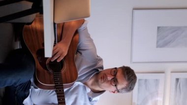 Dikey video. Müzik dersi. Akortlar çalışıyor. Çevrimiçi toplantı. Dizüstü bilgisayarda internet kursunda akustik gitar çalma kurallarını açıklayan profesyonel bir adamdan esinlendim..