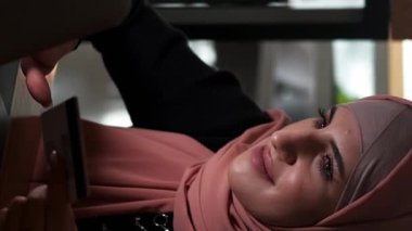 Dikey video. Çevrimiçi ödeme. İnternet alımı. Tesettürlü, tesettürlü bir kadın, kahve dükkanından kredi kartı e-ticaret para transferiyle laptoptan sipariş veriyor..