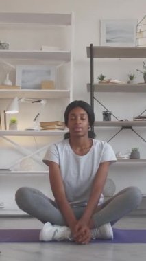 Dikey video. Sabah meditasyonu. Ev aktivitesi. Sportif hobi. Aktif giyimli, gevşemiş, ince kadın içeride spor minderinde yoga pozisyonu alıyor..