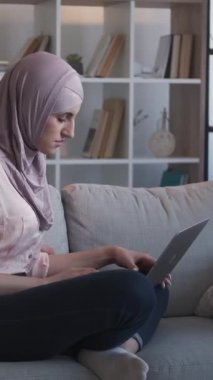 Dikey video. İnternet taraması. Uzaktan kumanda. Sakin kadın serbest sörf yapıyor. Ev oturma odasındaki rahat kanepede dizüstü bilgisayarla yazı yazıyor..