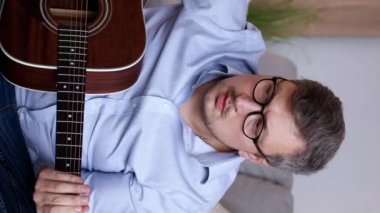 Dikey video. Gitar hobisi. Alet çalışması. Akıllı yaratıcı adam akustik telli melodi çalmayı öğreniyor evde eğitim becerileri.