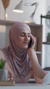 Dikey video. Cep telefonu konuşması. İş görüşmesi. Mutlu kadın yönetici telefonda konuşuyor. Ev ofis masaüstünde mobil şirket iletişiminin keyfini çıkarıyor..