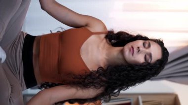 Dikey video. Meditasyon pratiği. Yoga gevşemesi. Huzurlu, güler yüzlü bir kız nilüfer çiçeğiyle bacak bacak üstüne atarak dinlenme egzersizinden zevk alıyor..