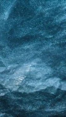 Dikey video. Işıltılı girdap. Suyu boya. Kar fırıldağı. Parlak mavi renkli sis, koyu kaba dokuda yüzen parlak toz parçacıkları soyut sanat arkaplanı.