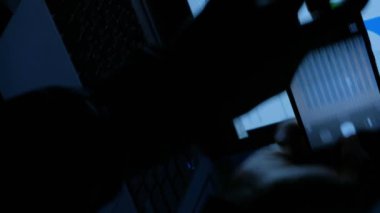 Dikey video. Ofis sahtekarı. Veri hırsızlığı. İşyeri bilgisayarında gece geç saatlerde akıllı telefondan kurumsal gizli proje bilgi istatistiklerinin fotoğrafını çeken adam elleri.