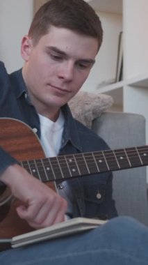 Dikey video. Gitarist. Şarkı sözü yazarı eğlencesi. Müzisyen yaşam tarzı. Evdeki kanepede telli çalgılar besteleyen yetenekli bir sanatçı ilham verdi..