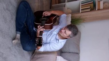 Dikey video. Gitar keyfi. İlham perisi. Sıradan bir adam yerde oturup akustik enstrüman çalıyor. Oturma odasının içinde, fotokopi odasının içinde en sevdiği melodi çalıyor..