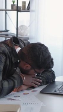 Dikey video. Yorgun çalışan. Son teslim tarihi. Aşırı çalışma yorgunluğu. Uykulu, yorgun, stresli adam iş belgelerinde kestiriyor. Laptop ofisinde dinleniyor..