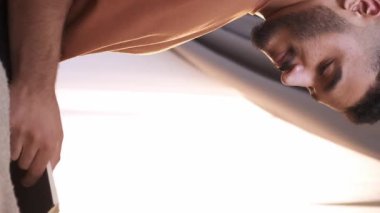 Dikey video. Okuma öğrenme. Ev tatili. Bilgi eğitimi için. Açık kitabı olan rahat zeki bir adam fotokopi aletiyle ışık penceresinde sayfaları çeviriyor..