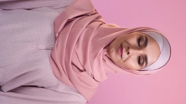 バーティカルビデオ イスラムの女性の肖像画 ポジティブな感情 ハッピー楽観的な陽気な美しい女性の顔ヒジャブのヘッドスカーフは ピンクで孤立しました — ストック動画