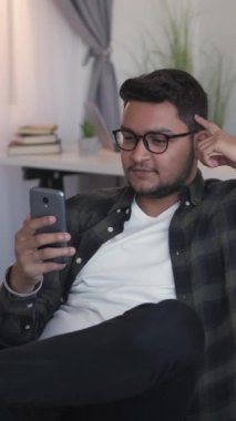 Dikey video. Çevrimiçi çağrı. Sanal iletişim. Cihaz eğlencesi. Neşeli bir adam cep telefonuyla konuşuyor. Sosyal medya, internet, rahat bir kanepede sohbet ediyor..