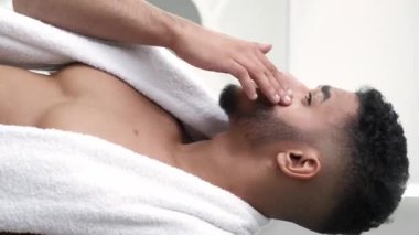 Dikey video. Cilt nemlendirici. Yüz bakımı. Sabah rutini. Havluyla banyodan sonra yüz kremi süren kendinden emin bir adam..