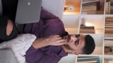 Dikey video. İnternet sohbeti. Webinar işi. Çevrimiçi görüşme. Kendine güvenen erkek koç modern iç mekandaki koltukta dizüstü bilgisayar kullanarak konuşuyor..